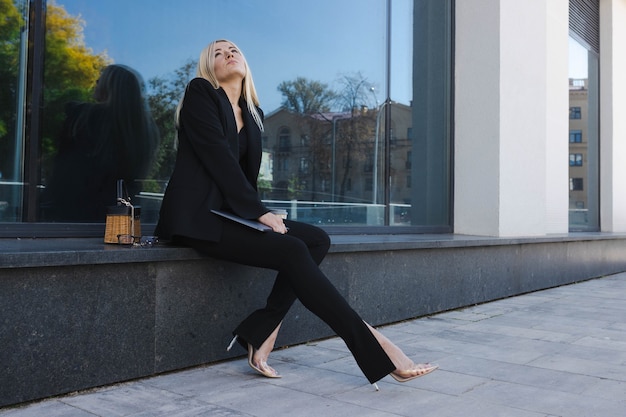 Una mujer joven con un elegante traje está sentada en la calle