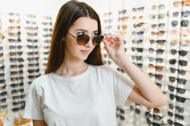 Una mujer joven elige gafas de sol en una tienda de óptica