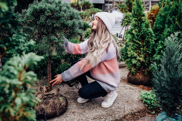 Mujer joven eligiendo un árbol de Navidad en invernadero