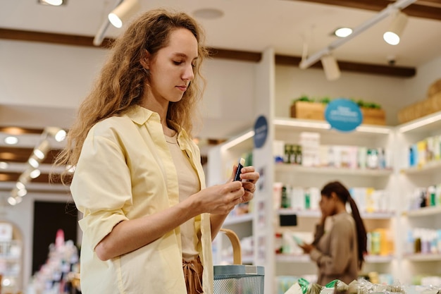 Mujer joven eligiendo lápiz labial durante las compras en la tienda de cosméticos