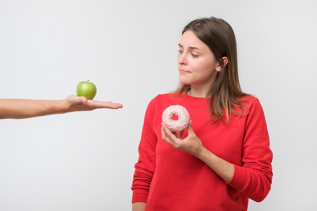 Mujer joven eligiendo entre manzana y donut