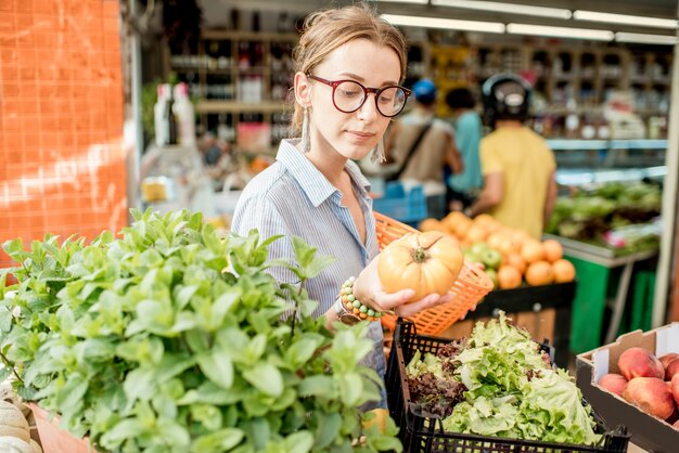 Mujer joven eligiendo un tomate fresco de pie con canasta en el mercado de alimentos en Francia