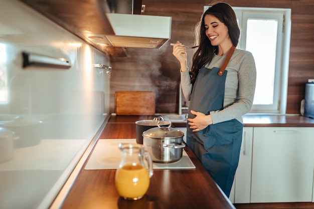 Mujer joven embarazada preparando una comida en la estufa en casa