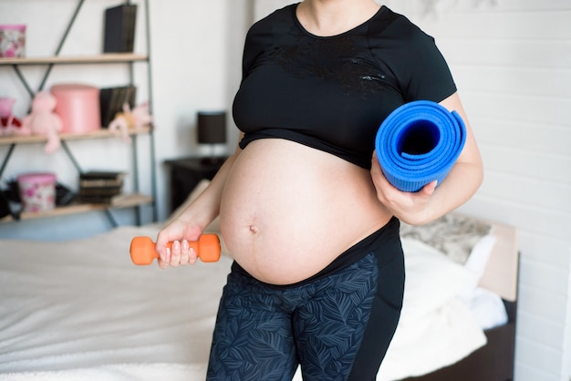 Mujer joven en embarazo con esterilla enrollada en su brazo yendo a clase de yoga prenatal.