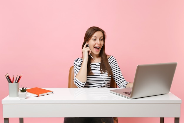 Mujer joven emocionada con auriculares escuchando música haciendo videollamadas sentarse trabajar en la oficina con un portátil pc contemporáneo