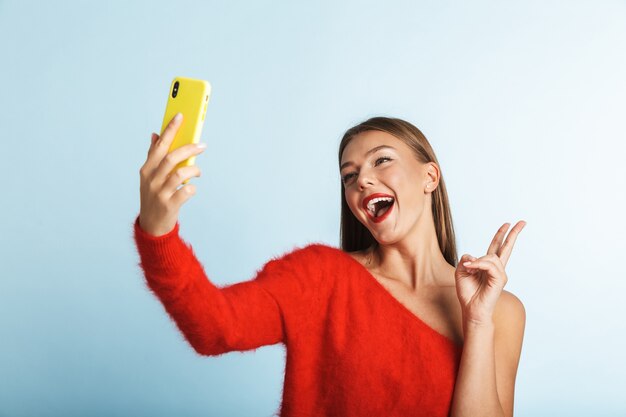 Mujer joven emocionada emocional que presenta aislada, tomar un selfie por teléfono móvil.