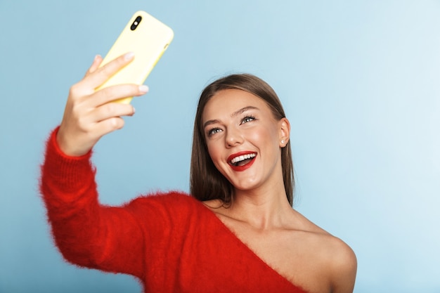 Mujer joven emocionada emocional que presenta aislada, tomar un selfie por teléfono móvil.
