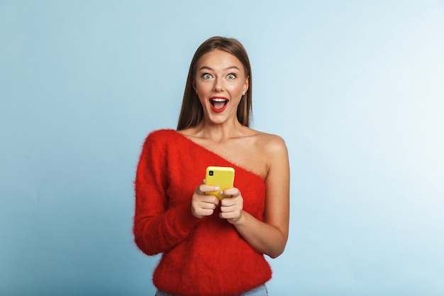 Mujer joven emocionada emocional que presenta aislada, usando el teléfono móvil.