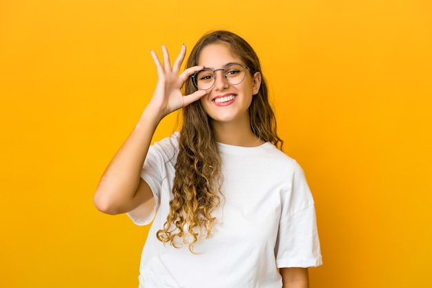Mujer joven emocionada manteniendo el gesto ok en el ojo