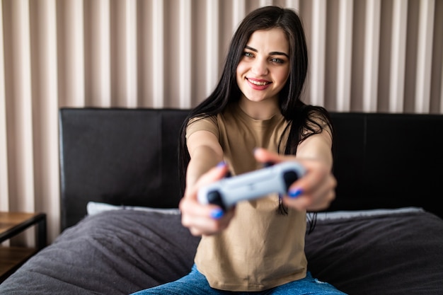 Mujer joven emocionada que sostiene el controlador de joystick gamepad jugando videojuegos sentado en el sofá en casa.