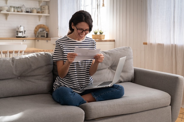 Mujer joven emocionada sentarse en el sofá en casa recibiendo trabajo disfrutar de los resultados del examen o carta de admisión a la universidad