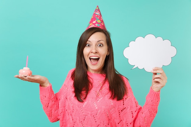 Mujer joven emocionada con sombrero de cumpleaños sostenga la torta en la mano con vela en blanco vacío Diga el bocadillo de diálogo de nube para contenido promocional aislado sobre fondo azul. Concepto de estilo de vida de personas. Simulacros de espacio de copia.