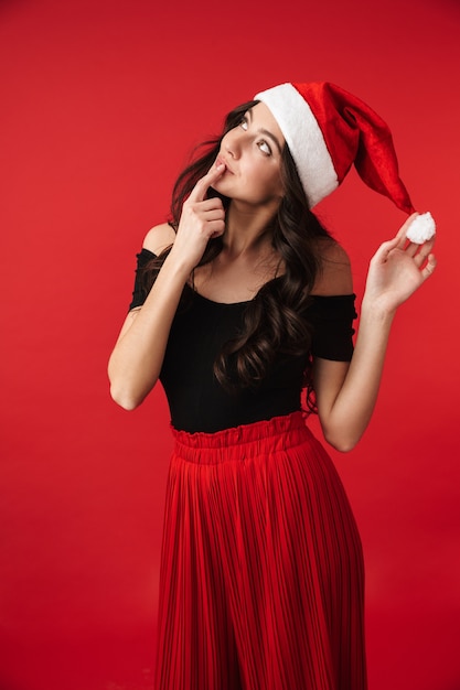 Mujer joven emocionada con sombrero de Navidad que se encuentran aisladas sobre rojo, posando