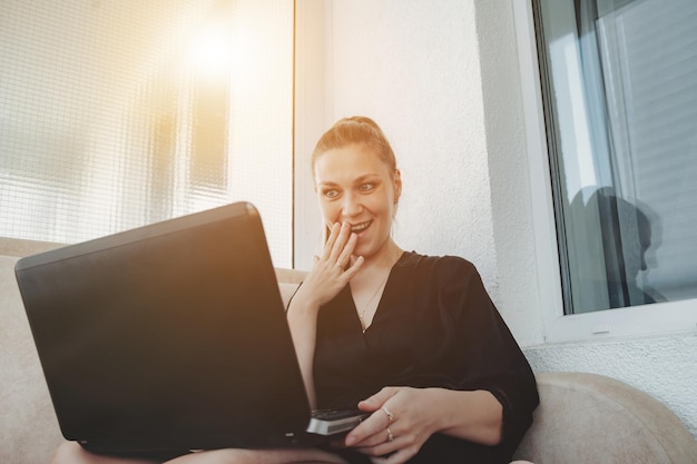 Mujer joven emocional que usa una computadora portátil en casa trabajo distante compras en línea o educación chat en redes sociales