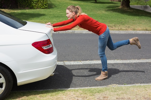 Mujer joven empujando su coche averiado