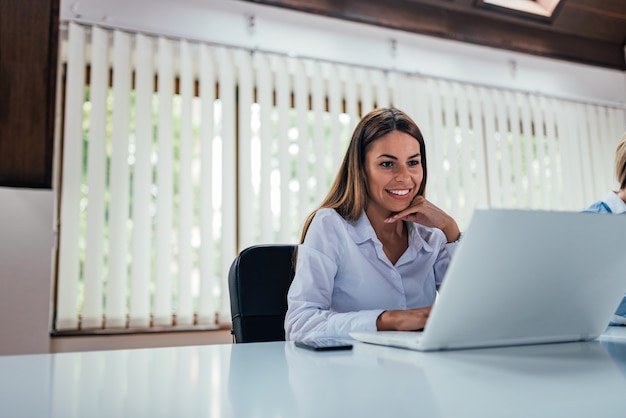 Mujer joven encantadora que trabaja en la computadora portátil en oficina coworking.