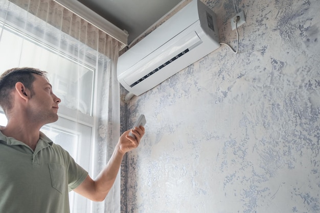 Mujer joven encendiendo el aire acondicionado en casa para la temperatura de confort con control remoto en h