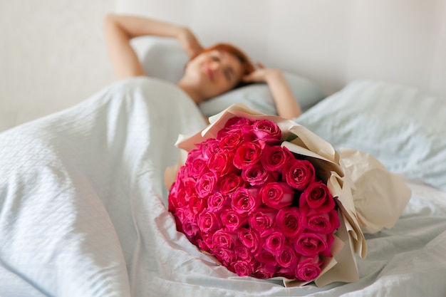 Mujer joven encontró ramo de rosas con joyas en caja de regalo en la cama. Niña feliz que huele a flores. Sorpresa del día de San Valentín