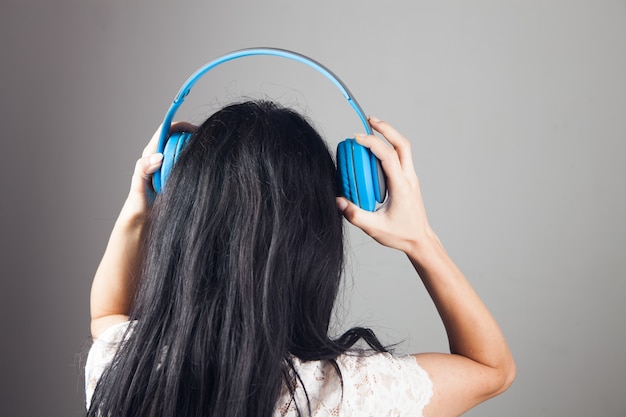 Mujer joven se encuentra en auriculares grandes sobre un fondo gris