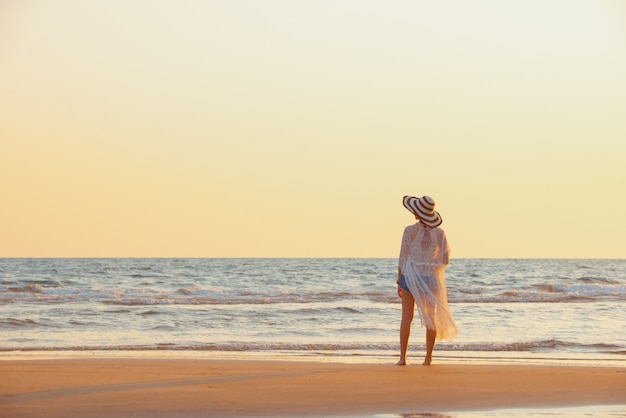 Una mujer joven se encuentra en la playa durante una puesta de sol, vacaciones de verano.