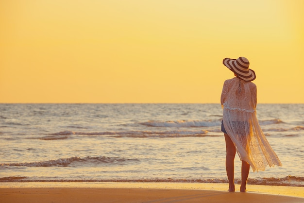 Una mujer joven se encuentra en la playa durante una puesta de sol, vacaciones de verano.