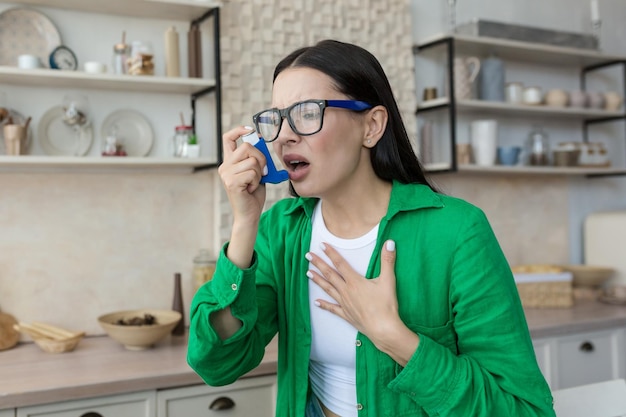 Mujer joven enferma en casa con asma usando un inhalador para facilitar la respiración y el tratamiento de la morena en