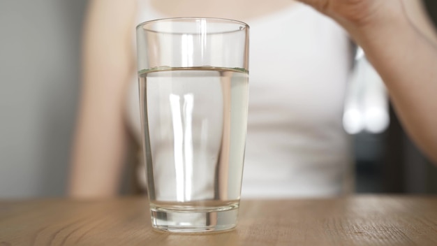 Mujer joven enferma que cae la tableta efervescente en un vaso de agua.