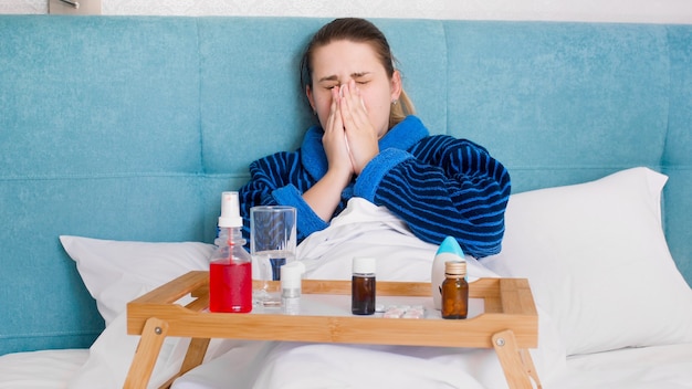 Mujer joven enferma con resfriado acostado en la cama con una gran cantidad de medicamentos y pastillas.