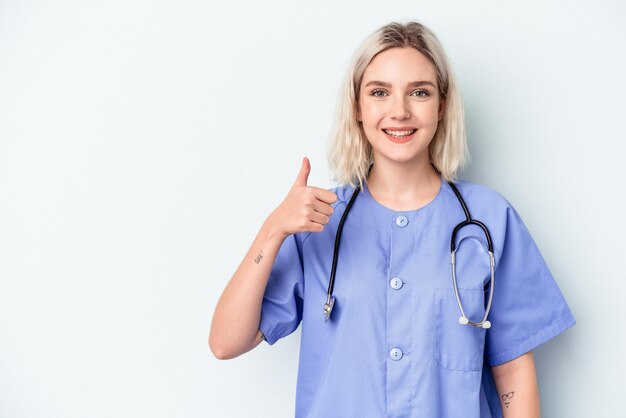 Mujer joven enfermera aislada sobre fondo azul sonriendo y levantando el pulgar hacia arriba