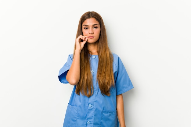 Mujer joven enfermera caucásica con los dedos en los labios manteniendo un secreto.