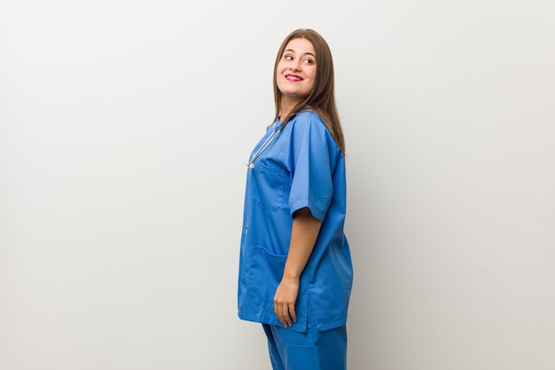 Mujer joven enfermera contra una pared blanca mira a un lado sonriente, alegre y agradable.