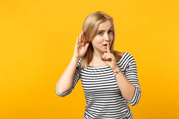 Mujer joven engañosa tratando de escucharte, diciendo silencio, silencio con el dedo en los labios, gesto shhh aislado en el fondo de la pared naranja amarilla. Emociones sinceras de la gente, concepto de estilo de vida. Simulacros de espacio de copia.