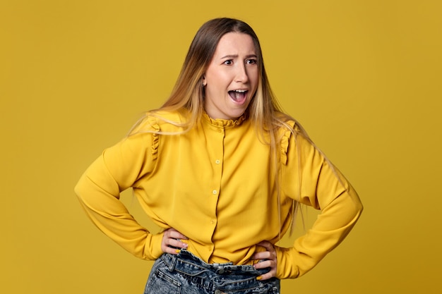 Mujer joven enojada gritando sobre fondo amarillo.