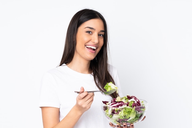 Mujer joven con ensalada en la pared blanca