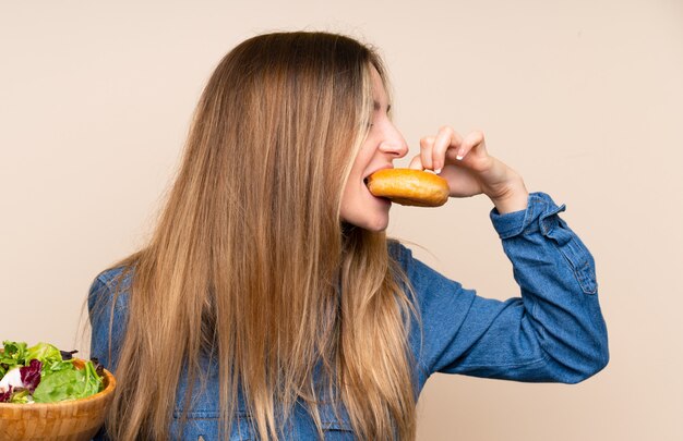 Mujer joven con ensalada sobre aislado y sosteniendo un donut