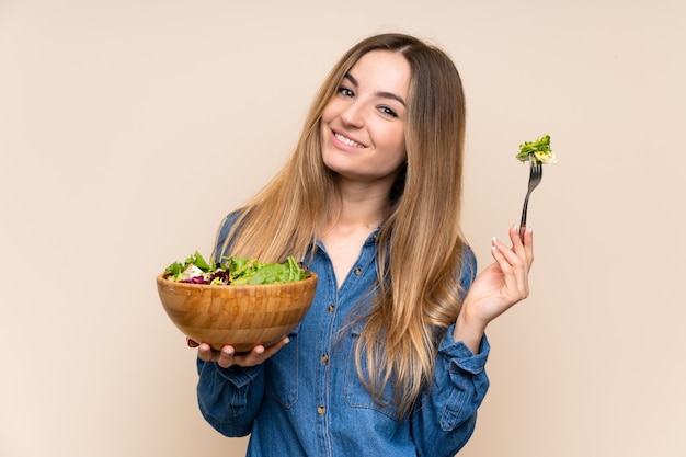 Mujer joven con ensalada sobre pared aislada