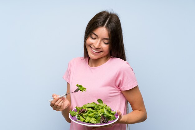 Mujer joven con ensalada sobre pared azul aislada