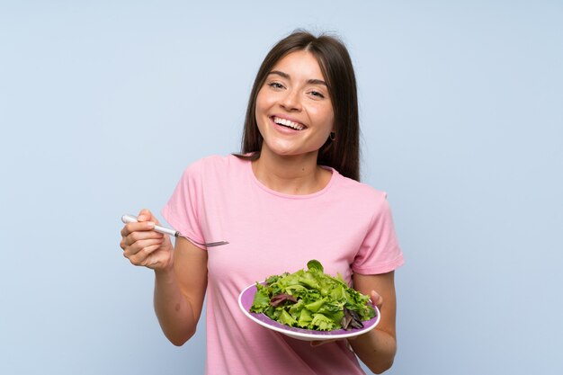 Mujer joven con ensalada sobre pared azul aislada