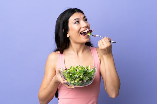 Mujer joven con ensalada sobre pared púrpura aislado