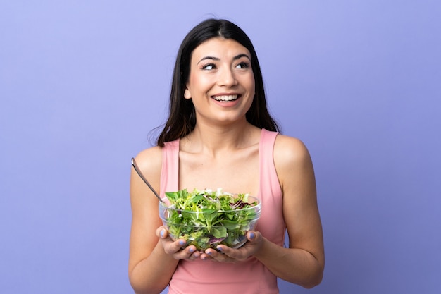 Mujer joven con ensalada sobre pared púrpura