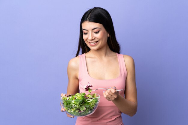 Mujer joven con ensalada sobre pared púrpura