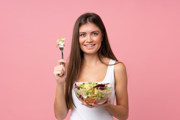 Foto mujer joven con ensalada sobre pared rosa aislado