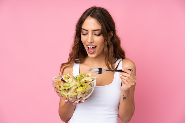 Mujer joven con ensalada sobre pared rosa