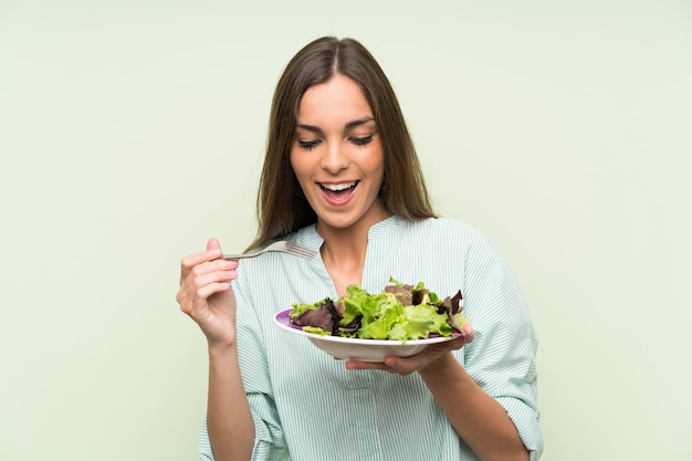 Mujer joven con ensalada sobre pared verde aislado