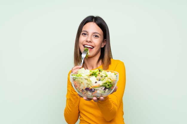 Mujer joven con ensalada sobre pared verde aislado