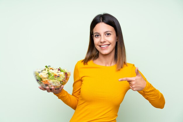 Mujer joven con ensalada sobre pared verde aislado