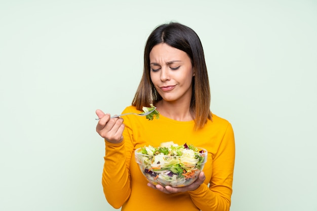 Mujer joven con ensalada sobre pared verde aislado