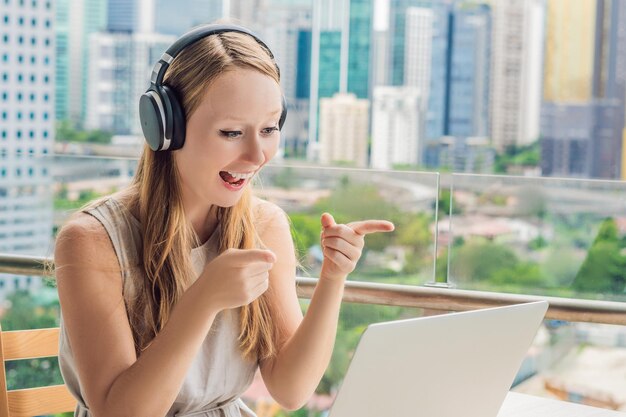 Mujer joven enseña un idioma extranjero o aprende un idioma extranjero en Internet en su balcón con el telón de fondo de una gran ciudad. Estilo de vida de la escuela de idiomas en línea