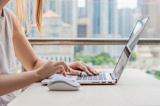 Mujer joven enseña un idioma extranjero o aprende un idioma extranjero en Internet en su balcón con el telón de fondo de una gran ciudad Estilo de vida de la escuela de idiomas en línea