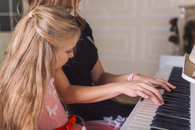 La mujer joven enseña a la niña a tocar el piano